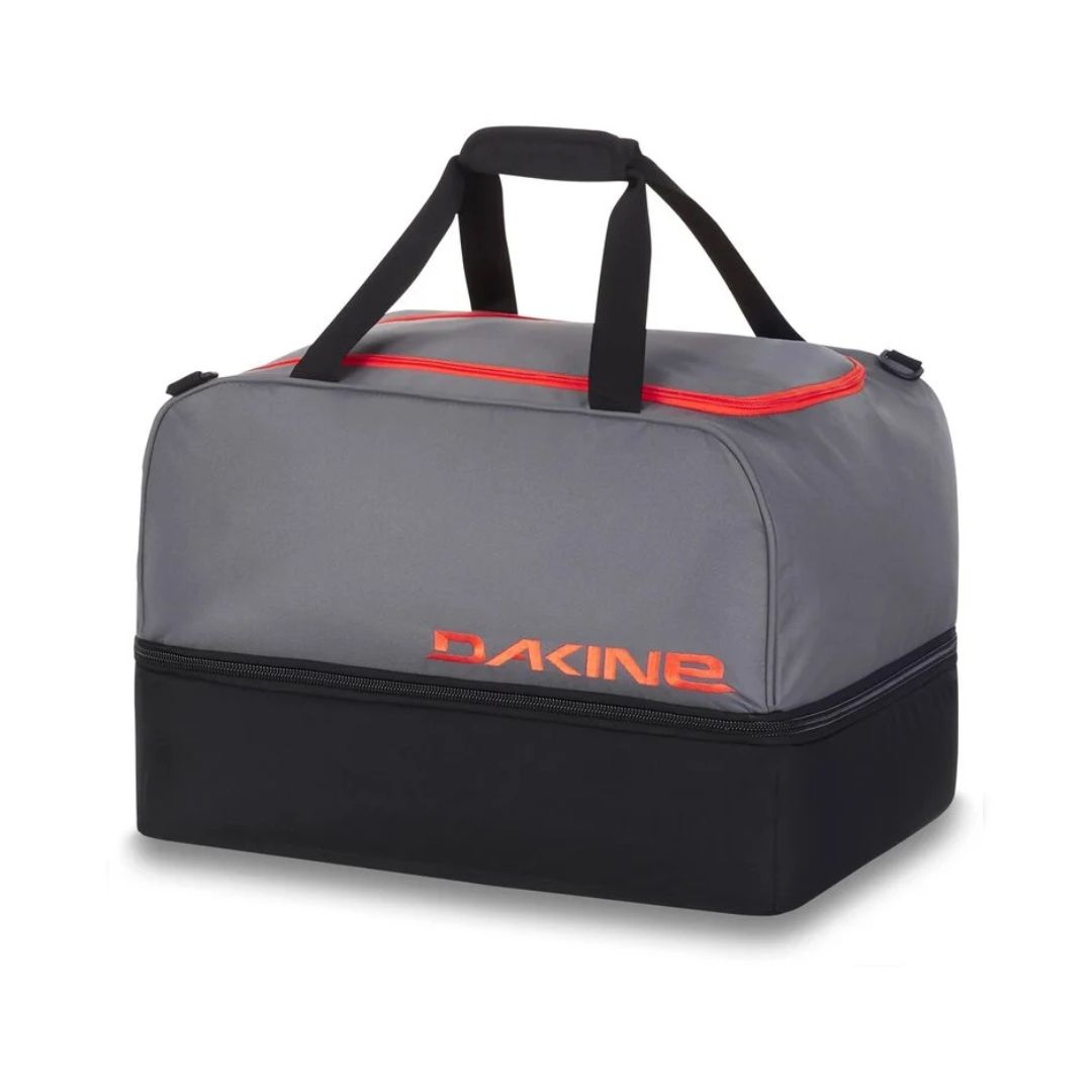 Sac de sport gris et noir avec des touches de rouge et le nom de la marque « Dakine » en lettres rouges. Il est doté de deux poignées noires et d'une forme rectangulaire avec un design spacieux.