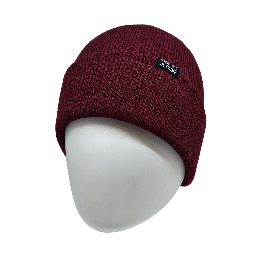 Un bonnet en tricot bordeaux avec un patch rectangulaire noir sur lequel est écrit « JE PEUX PAS J'AI » en texte blanc, placé sur une tête de mannequin blanche. Le bonnet semble confortable et douillet.