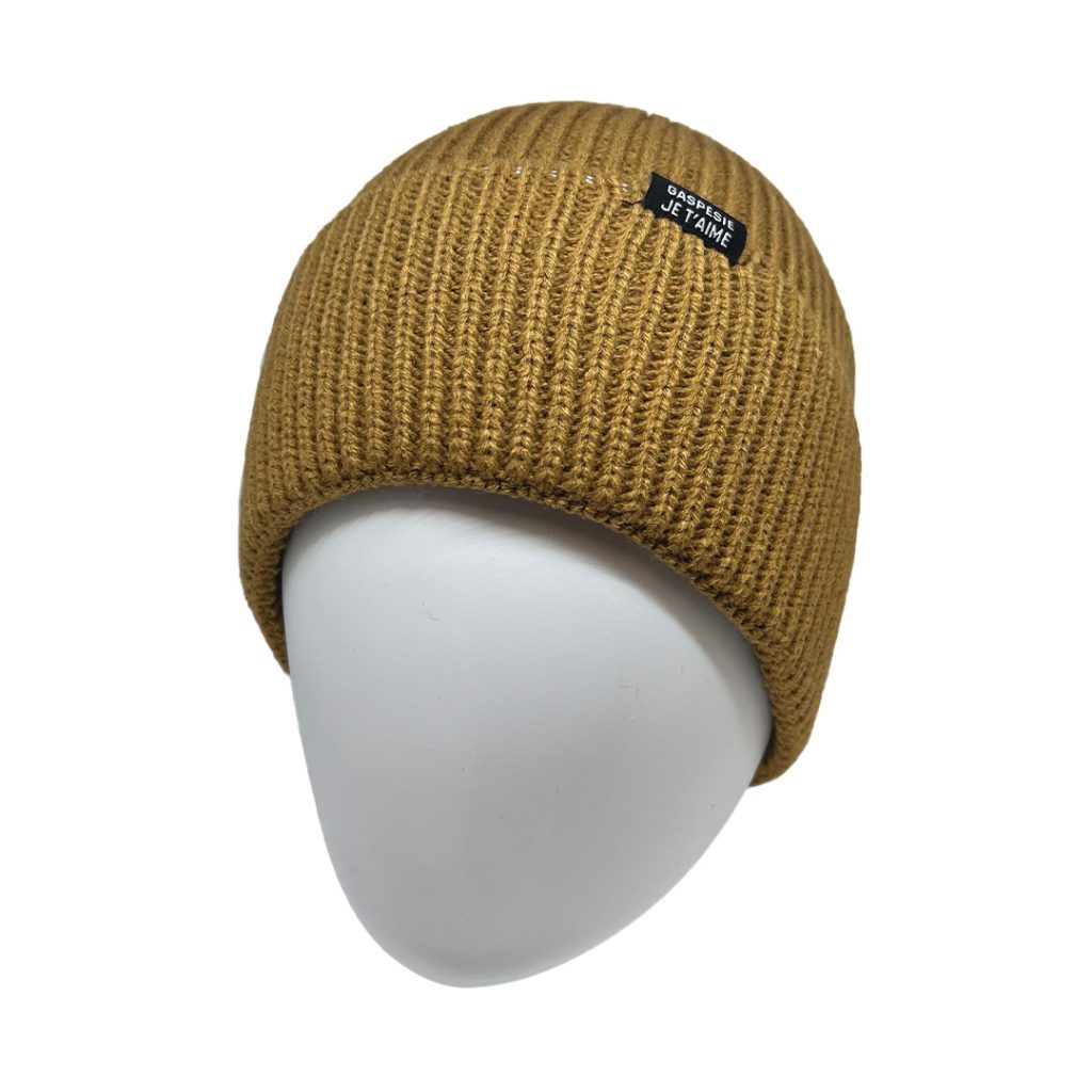 Une tête de mannequin portant un bonnet en tricot côtelé marron avec un petit patch rectangulaire noir sur lequel figure un texte blanc. Le fond est blanc uni.