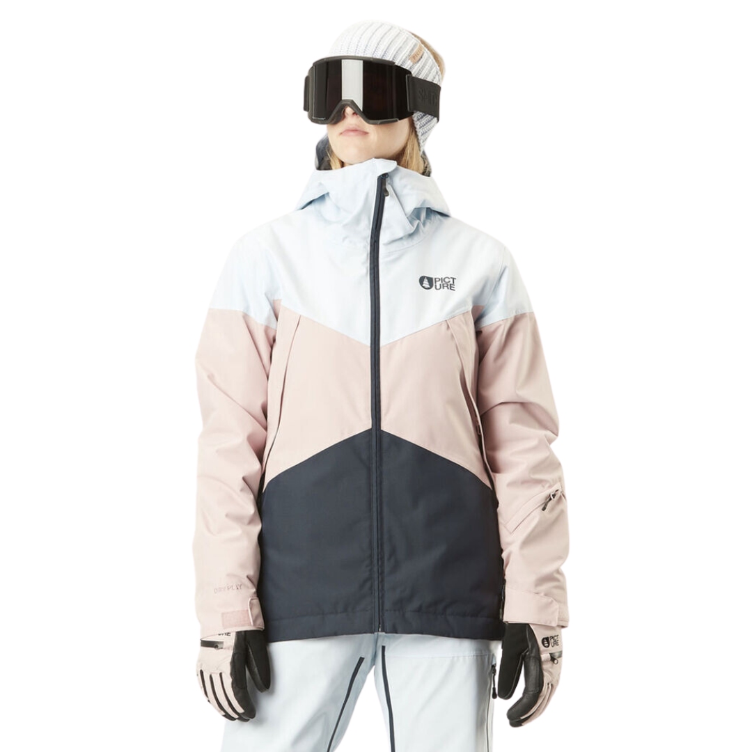 Une personne porte une veste d'hiver avec un motif à blocs de couleurs bleu clair, rose poudré et gris foncé sur fond blanc. Elle porte également des lunettes de ski, des gants et un bonnet.